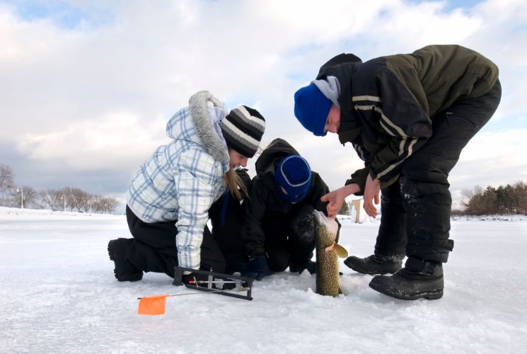 Kids pulling a large fish out of an ice hole while ice fishing on frozen Lake Michigan in Wisconsin